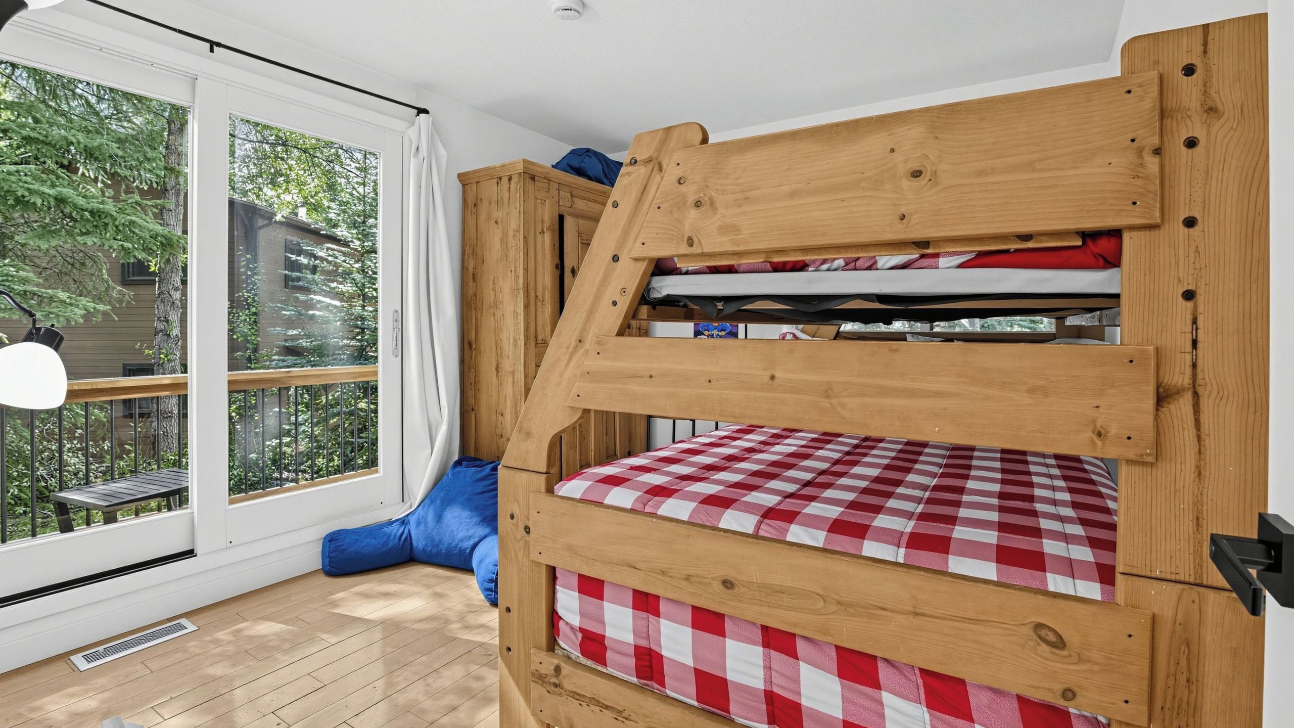 Ein Etagenbett mit einer karierten Matratze, einem blauen Kissen und einem Fenster mit Blick auf Grünflächen.