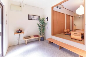 A room with a wooden bench, a potted plant, a wall-mounted shelf with a bowl, a mirror, and a wooden wardrobe. - Traditional House West Ikebukuro (Tokyo)