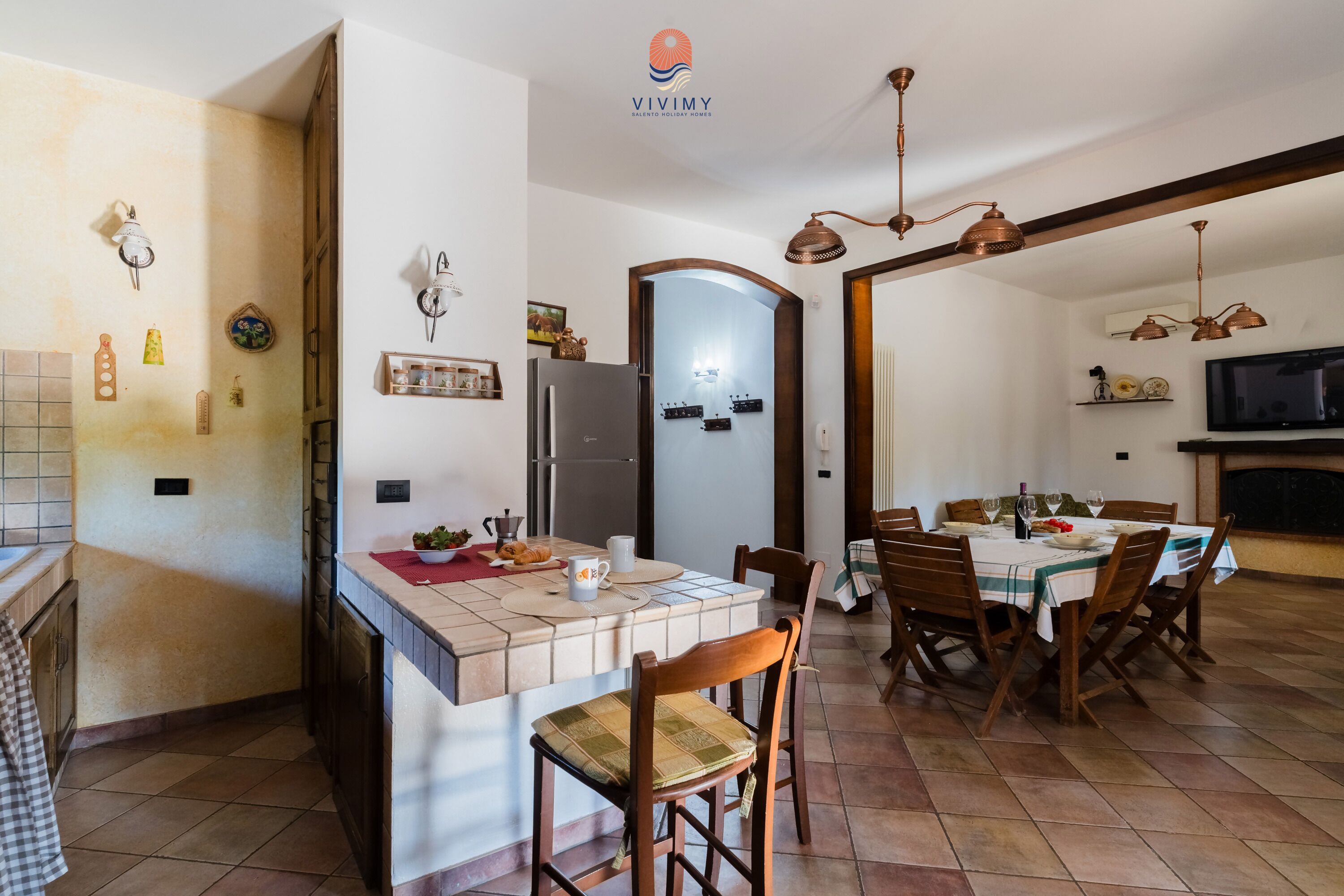 A kitchen with a central island, dining table, chairs, and a TV.