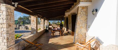 A covered patio area with stone walls, a wooden table with chairs, and a hammock.