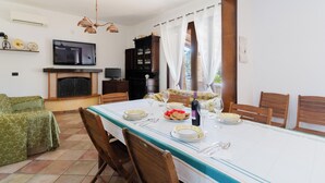 Ein Essbereich mit Tisch für vier Personen, einem Fernseher, einem Kamin und Blick durch ein Fenster.