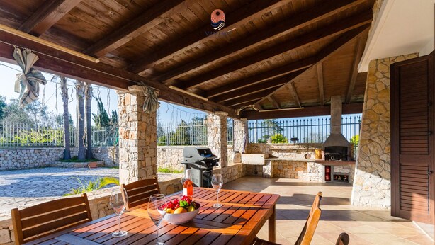 Eine Außenpatio mit Steinmauer, Holzmöbeln, Grill und Kamin aus Stein.