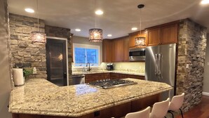 Uma cozinha com bancadas de granito, geladeira de aço inoxidável, armários de madeira e parede decorativa em pedra.