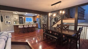 Uma cozinha moderna com painel de pedra, área de jantar com mesa e cadeiras de madeira, e escada que leva a um andar superior.