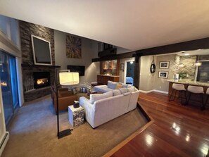 Amplia sala de estar con chimenea, un sofá, un televisor y una cocina al fondo.