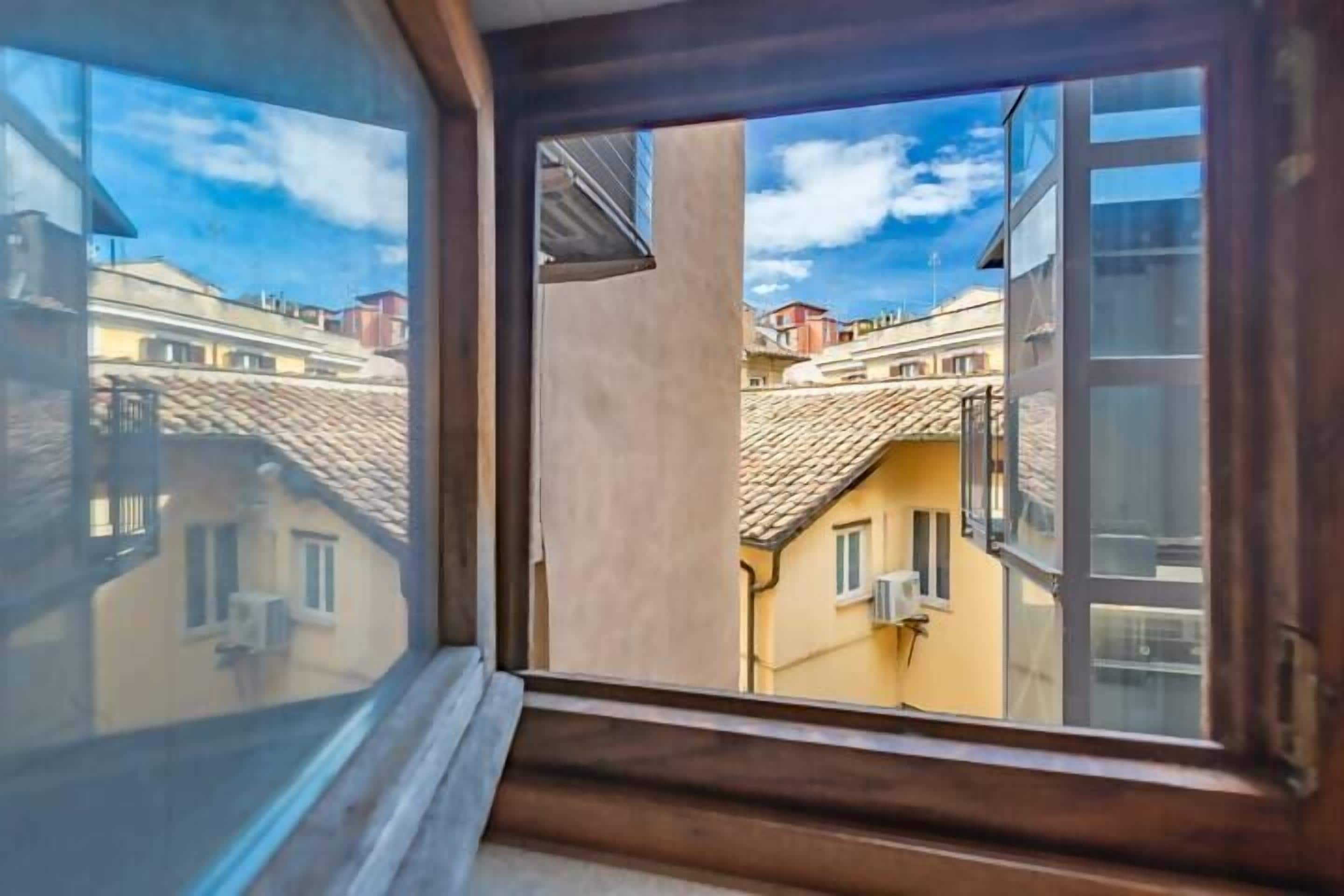 A window with a view of neighboring buildings and a clear sky.