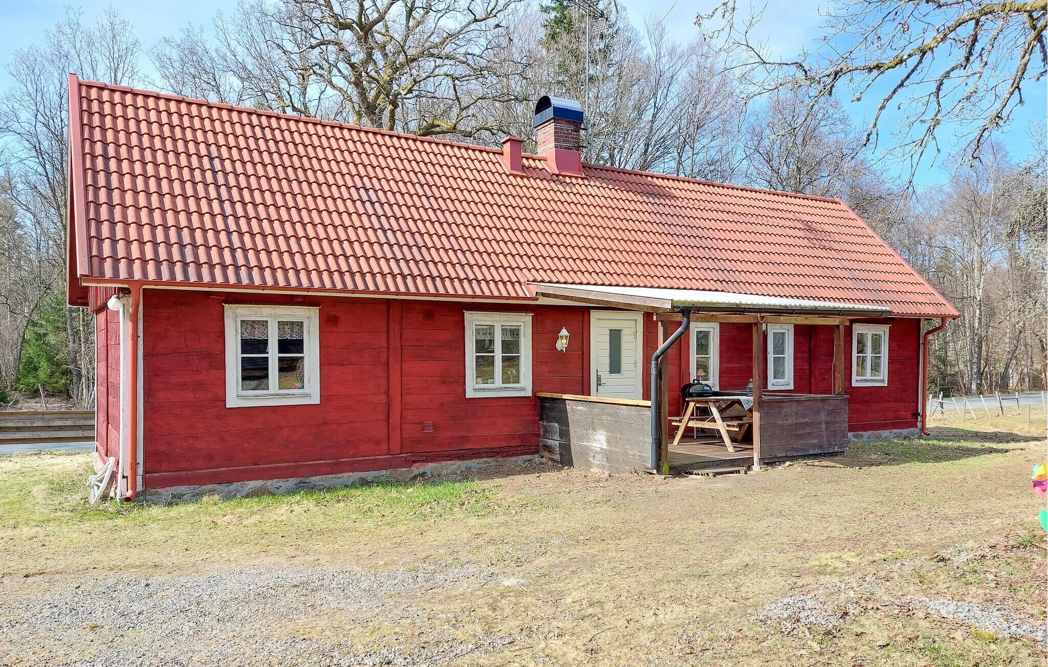 Une maison en bois rouge, avec un toit en tuiles, une cheminée et un petit porche agrémenté d’une table et de chaises.