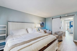 A bedroom with a bed, a nightstand, a chair, and a door leading to another room. - Oceanview condo with pool, hot tub, private balcony & direct beach access (North Myrtle Beach)