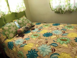 Een bed met bloemenbeddengoed, een groen hoofdeinde en patroon kussens.