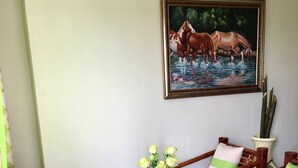 Quarto com cadeira e mesa de madeira, vaso com flores e pintura na parede.