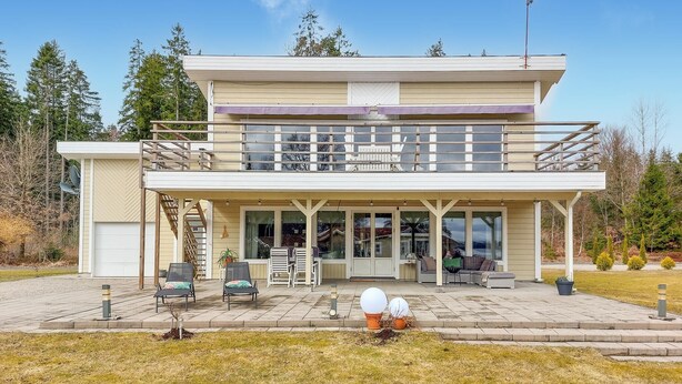 Ein zweistöckiges Haus mit überdachter Veranda, Sitzgelegenheiten im Freien und einer Satellitenschüssel.