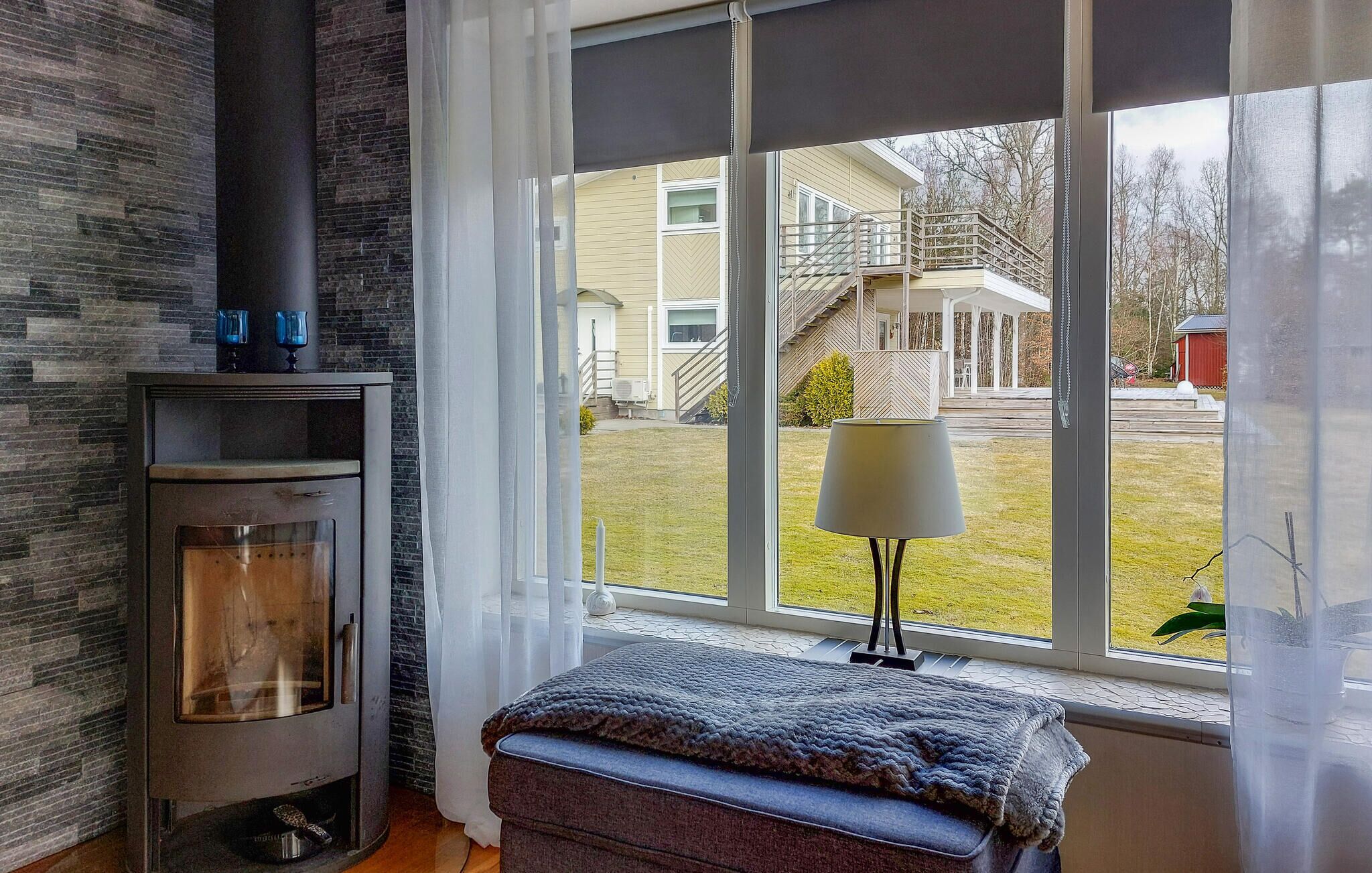 A room with a fireplace, a window with a view of a house, and a bench by the window.