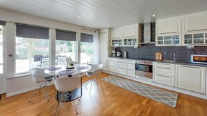 Eine moderne Küche mit weißen Schränken, einer zentralen Kochinsel mit Stühlen und Blick durch große Fenster.