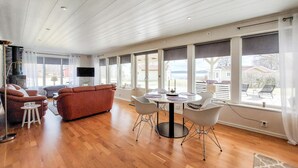 Ein geräumiger Wohnbereich mit einer Couch, einem Esstisch mit Stühlen und großen Fenstern mit Blick ins Freie.