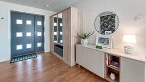 Ein Korridor mit einer dunklen Tür, einem Holzschrank, einem Spiegel, einem gerahmten Bild und einer Lampe.