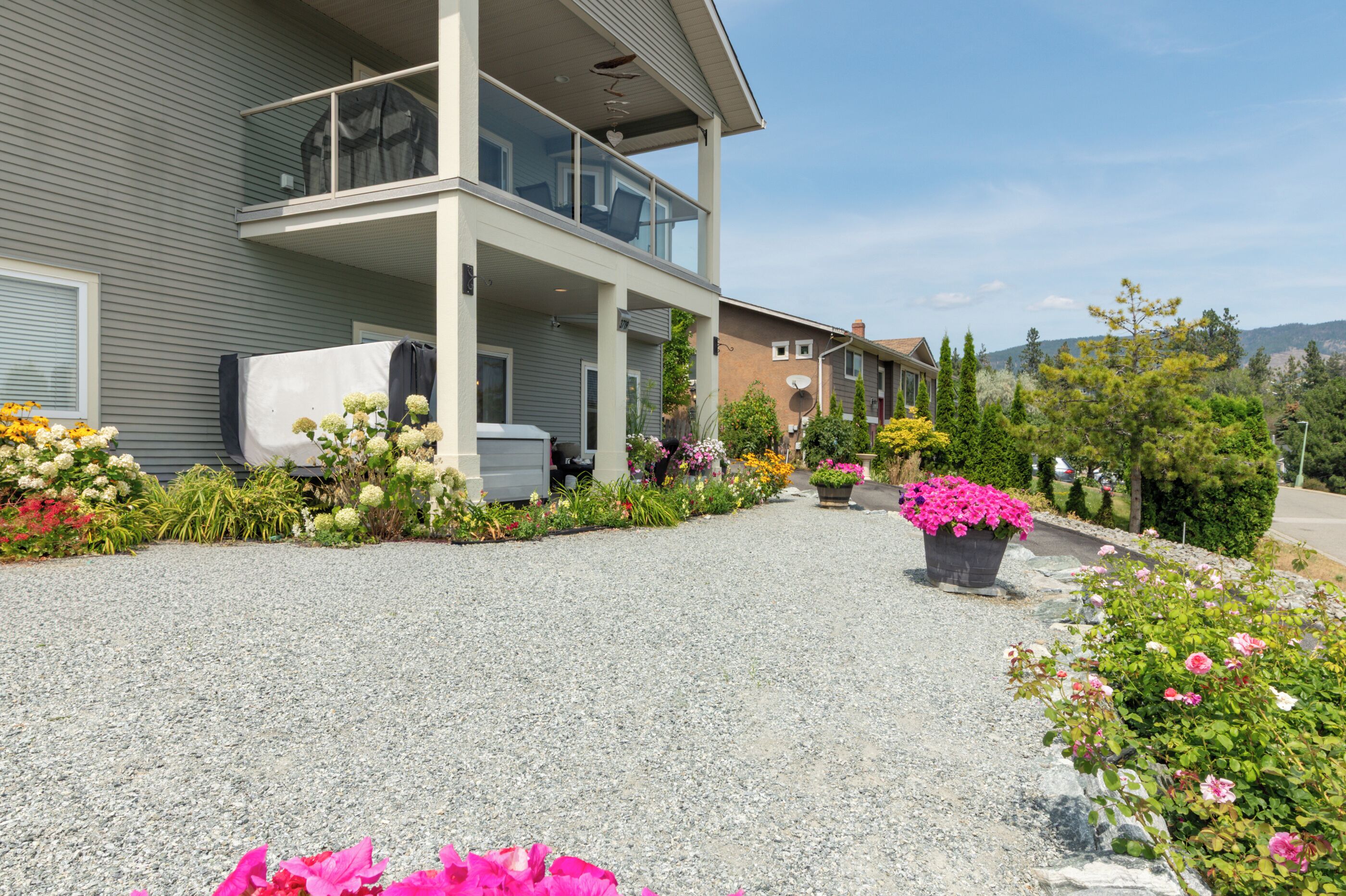 A two-story house with a covered porch, a gravel driveway, and various flowering plants.