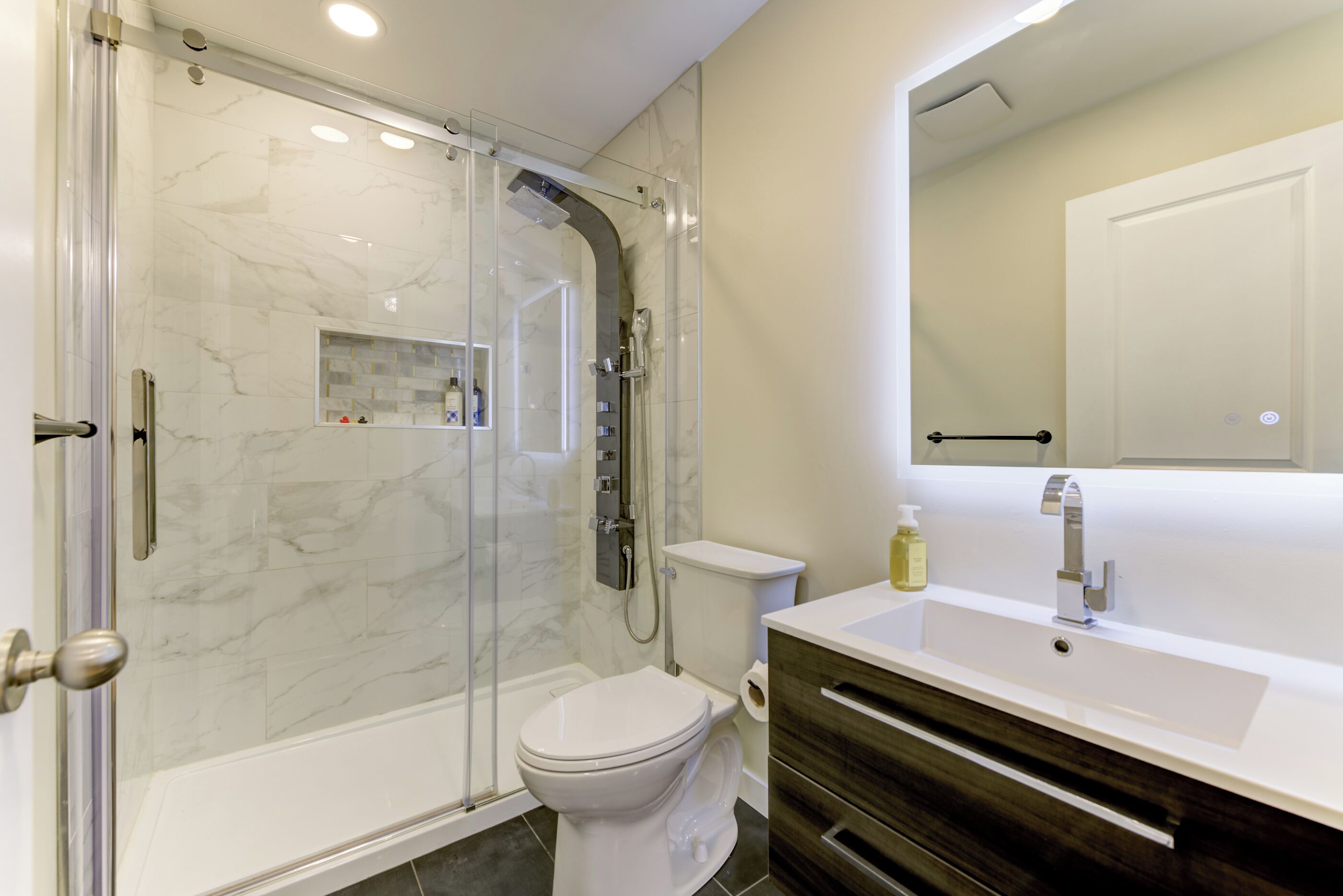 A modern bathroom with a glass-enclosed shower, a toilet, and a vanity with a mirror.