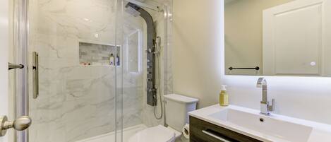 A modern bathroom with a glass-enclosed shower, a toilet, and a vanity with a mirror.
