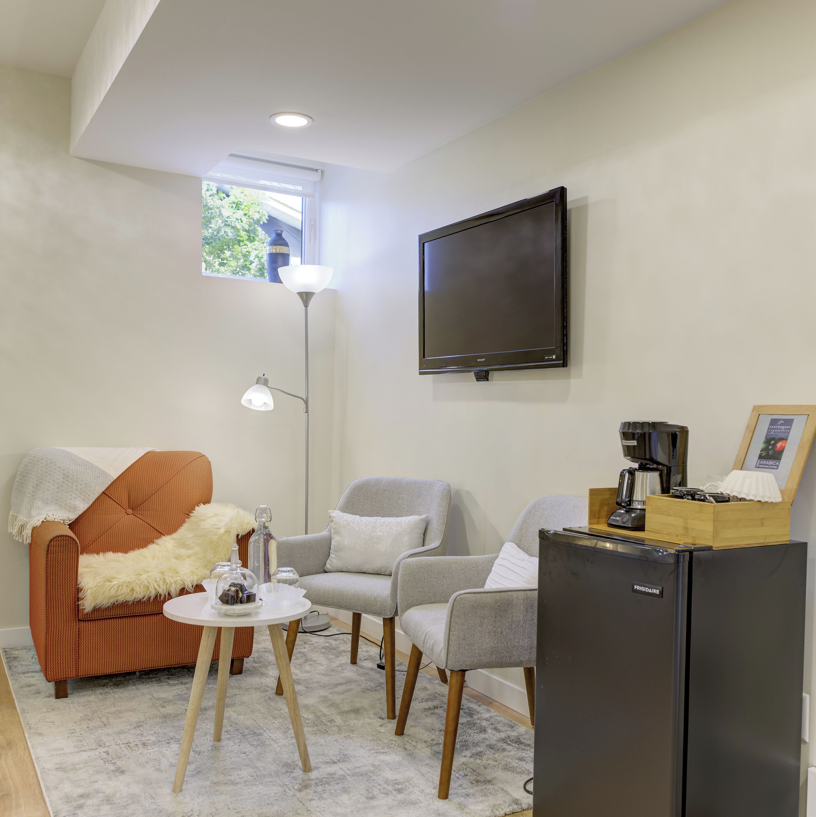 A modern living room with a sofa, armchairs, a coffee machine, and a TV mounted on the wall.