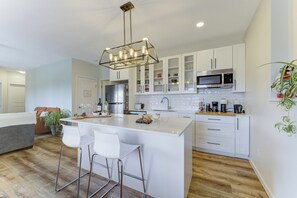 A modern kitchen with white cabinets, a stainless steel refrigerator, a microwave, and a bar area with stools.