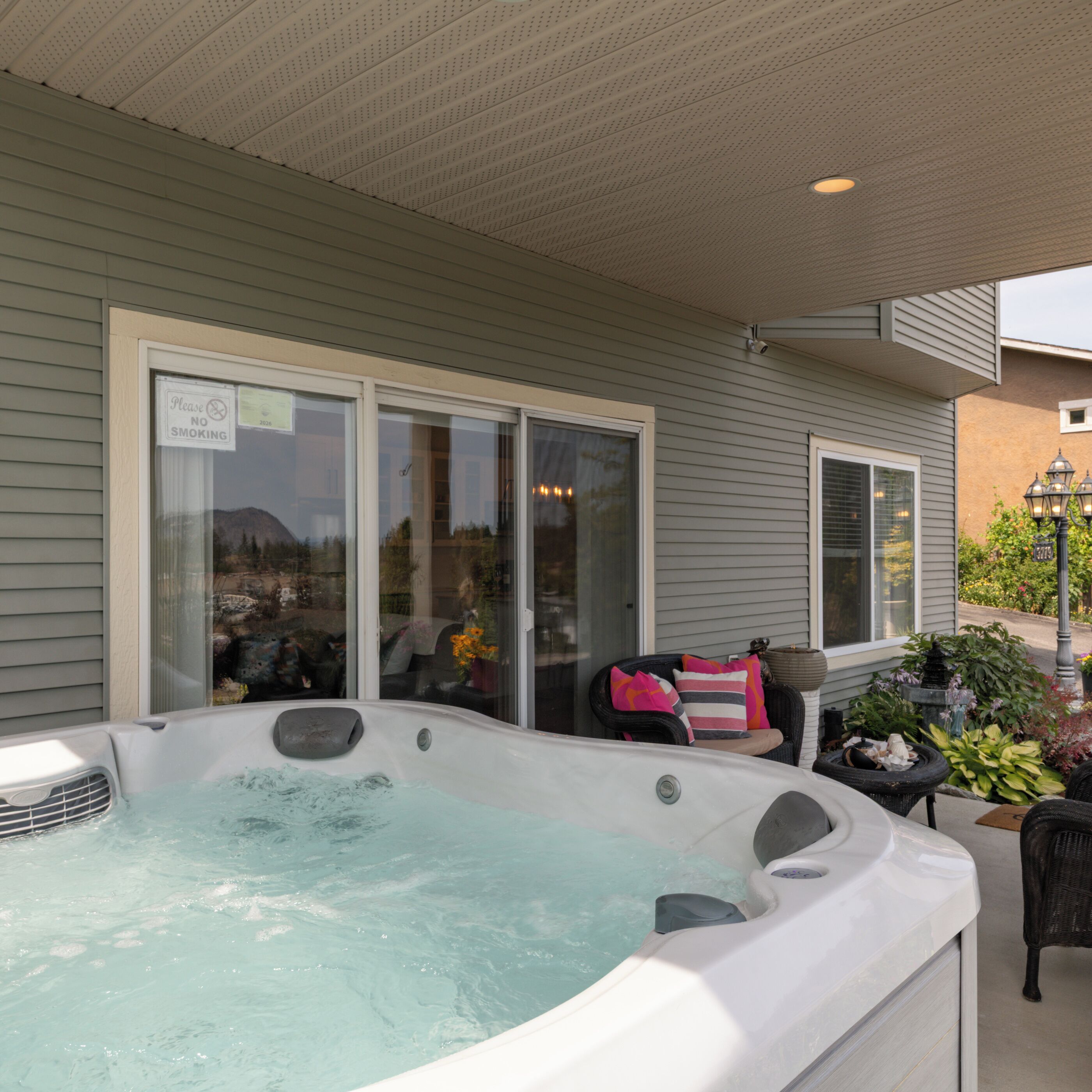Un jacuzzi en un patio con puerta corrediza de vidrio, una silla y plantas en macetas.