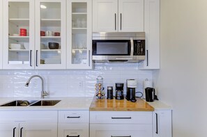 Una cocina con armarios blancos, un microondas de acero inoxidable, una cafetera y un lavabo.