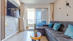 A modern living room with a grey sofa, a flat-screen TV, a marble wall, and a large window. - Beautiful apartment in Santa Marta closer to airport with view at the sea (Santa Marta City)