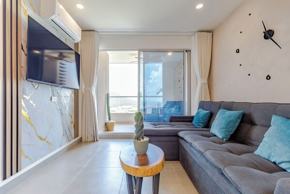 A modern living room with a grey sofa, a flat-screen TV, a marble wall, and a large window. - Beautiful apartment in Santa Marta closer to airport with view at the sea (Santa Marta City)