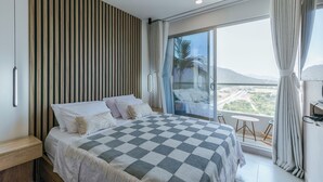 A modern bedroom with a large bed, a wooden slat wall, a balcony with a view, and a small table. - Beautiful apartment in Santa Marta closer to airport with view at the sea (Santa Marta City)