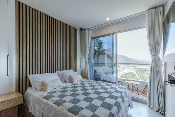Camera da letto moderna con un letto grande, una parete a doghe di legno, un balcone con vista e un piccolo tavolo.