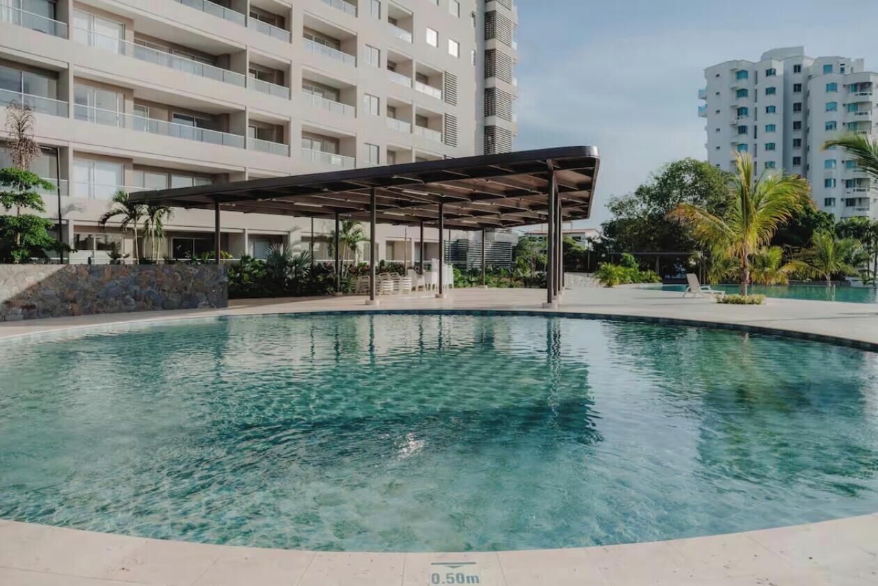 A swimming pool with a covered area, surrounded by a building with multiple balconies and a clear sky.