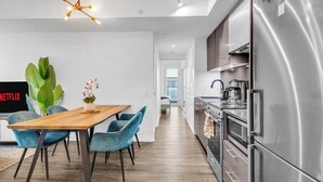 A modern kitchen with stainless steel appliances, a wooden dining table with blue chairs, and a large green plant.