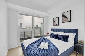 Un dormitorio moderno con una cama grande, vista a la ciudad a través de una puerta corredera y dos cuadros en la pared.