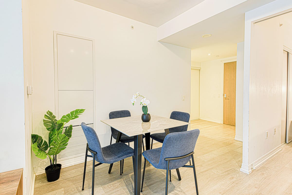 Un comedor con una mesa y sillas, una planta en maceta y una puerta al fondo.