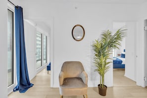 Una habitación con un ventanal grande, una silla, una planta en maceta y un espejo en la pared.