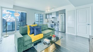A modern apartment with a green sofa, a glass coffee table, and a view of the city through large windows.