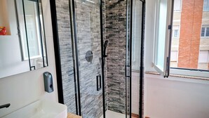 A modern bathroom with a glass shower enclosure, a white sink, and a window with a view of a brick building. - The houses of Vanda (Milano)