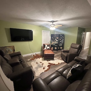 A living room with leather sofas, a flat-screen TV, a ceiling fan, and a cowhide rug. - Premier Executive Living | 4br Luxury Apartment (Evans)