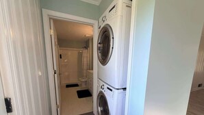 A laundry room with a washing machine and dryer, a door leading to a bathroom, and a patterned rug on the floor. - Spacious & Cozy 3BR | Perfect for Families (Augusta)