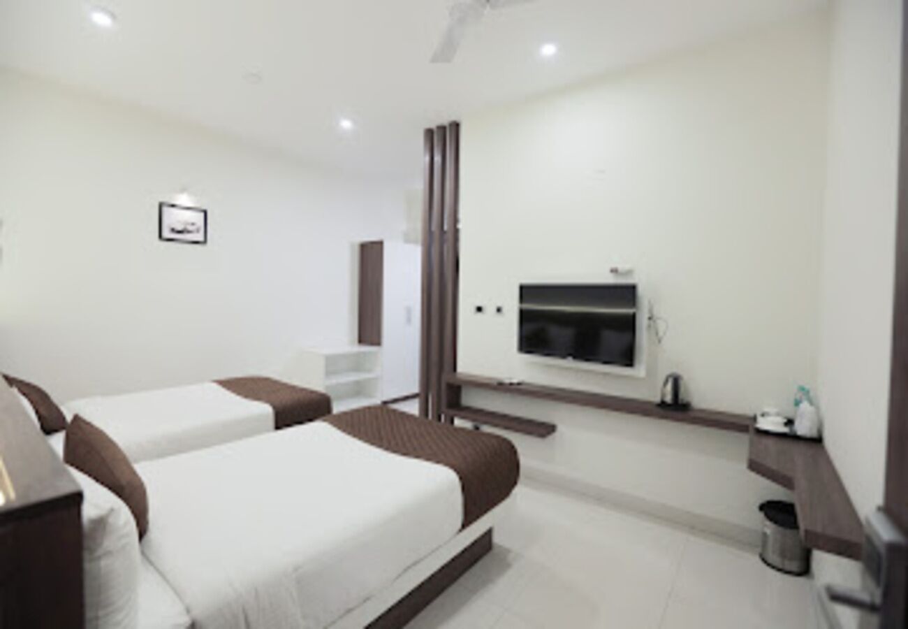 A hotel room with two beds, a TV, a small desk, and a trash can.