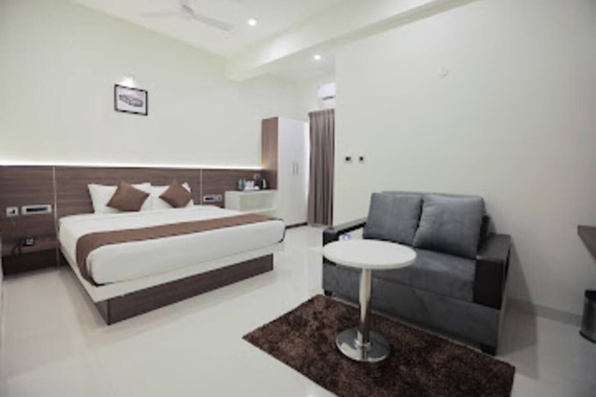 A modern hotel room with a bed, a gray sofa, a small round table, and a ceiling fan.