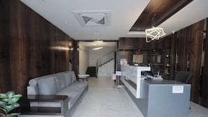 A reception desk, a grey sofa, a staircase, and a wooden wall. - Nandha Grande (Udumalaipettai)