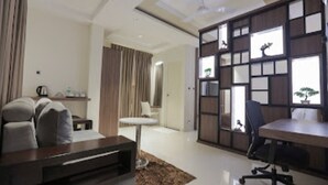 A modern living room with a sofa, a coffee table, a TV stand, a desk, and a chair. There is a large window with a view of the outside. - Nandha Grande (Udumalaipettai)