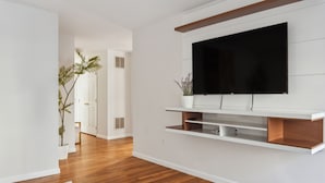 A modern living room with a flat-screen TV mounted on a white wall, wooden flooring, and a grey abstract rug.