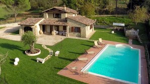 A villa with a swimming pool, a patio with lounge chairs, and a well-maintained lawn. - Umbria Genius Loci Farmhouse (Collazzone)