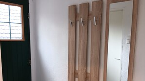 Una habitación con un banco de madera, una puerta y un espejo fijado a la pared.