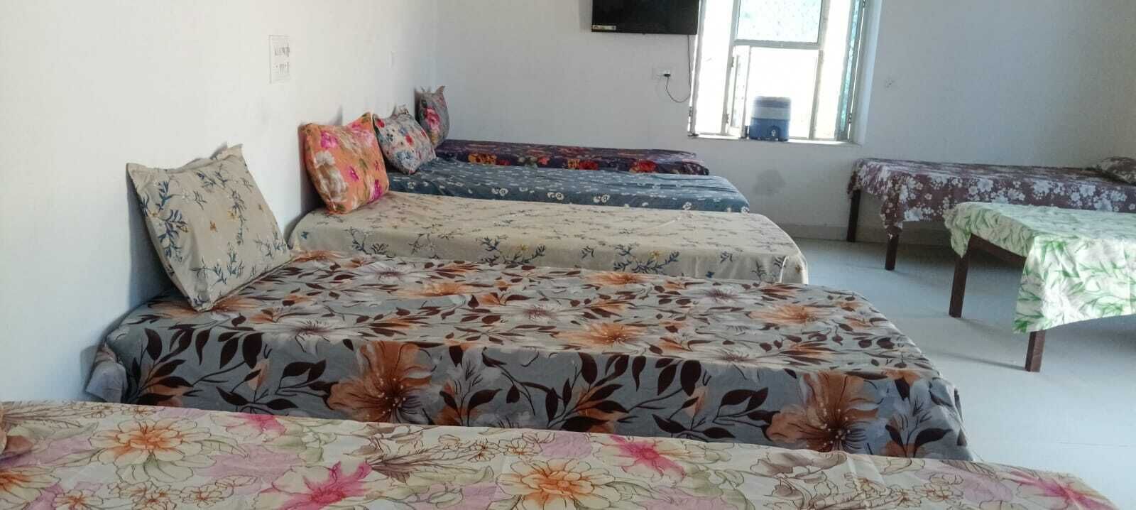 A room with three beds, each with floral bedding, a television on the wall, and a window with a view.