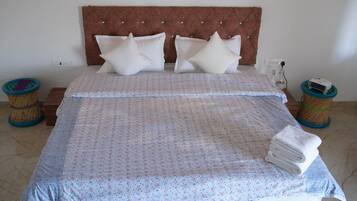 A neatly made bed with a patterned bedspread, two decorative pillows, and a stack of folded towels on a wooden nightstand.