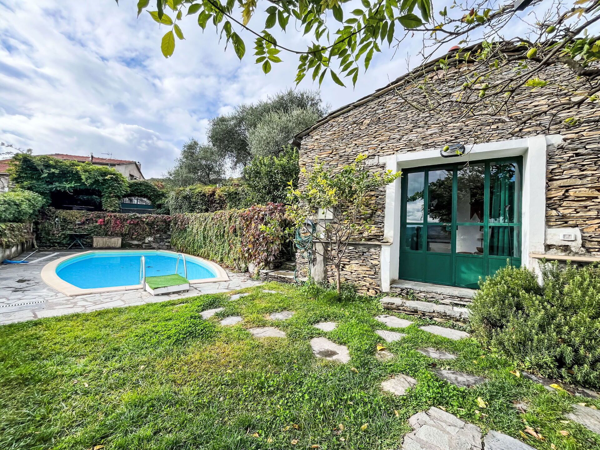 Un bâtiment en pierre doté d’une piscine, d’une porte verte et d’un chemin en pierre menant à la piscine.