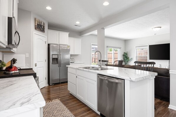 A modern kitchen with white cabinetry, a stainless steel refrigerator, a dishwasher, and a marble countertop.